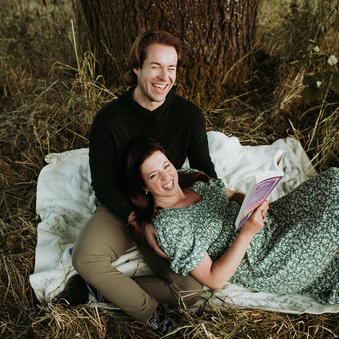 Man and woman sitting under a tree on a blanket in a natural setting