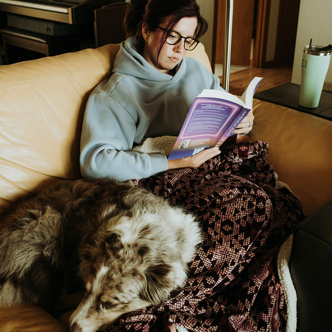 Woman reading a book on a couch with a dog next to her